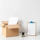 Kaksi muuttolaatikkoa, toisessa sopimus. Vieressä muistiinpanot ja avaimet. Minimalistinen sommittelu kuvastaa muuton suunnittelua.